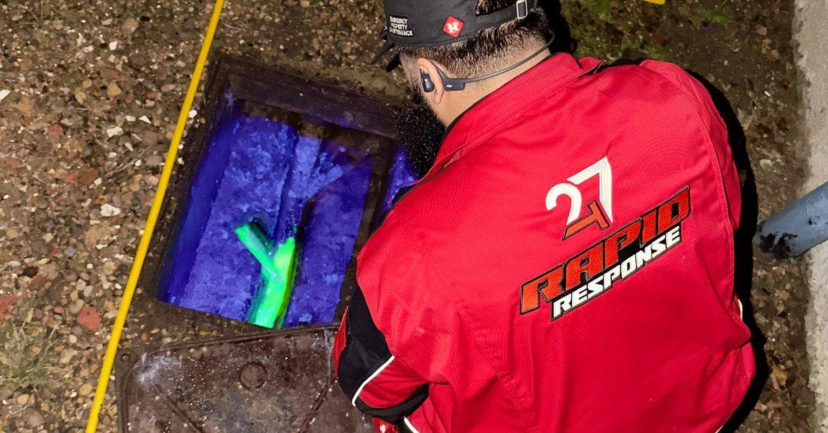 247 Rapid Response engineer surveying an open manhole at night with UV dye visible in the chamber for blockage tracing